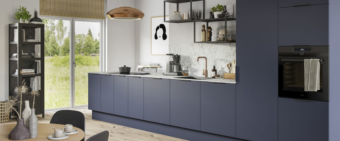 Blå, moderne kjøkkeninnredning med slette overflater og brede sokkellister montert. Ellers lyst rom med tregulv og detaljer i sort og messing. 