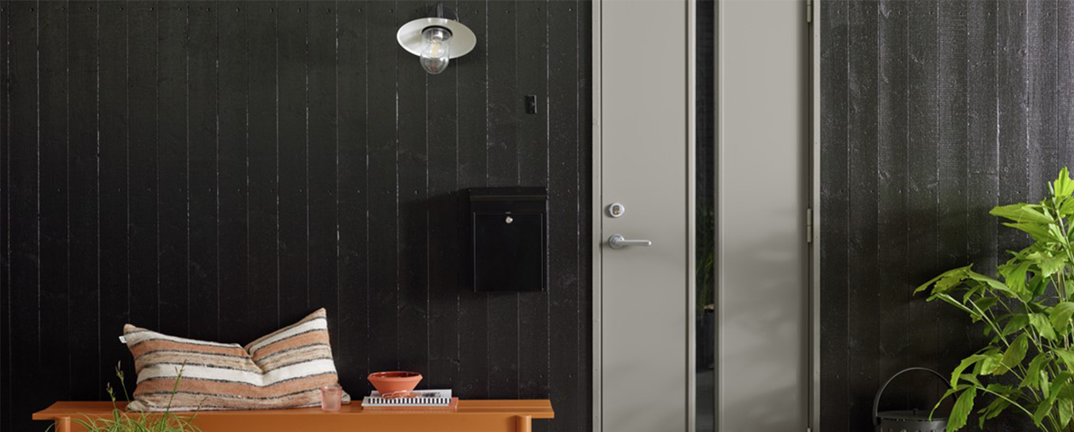 Lys grå ytterdør med smalt, vertikalt høyt glassparti til sortmalt husvegg.