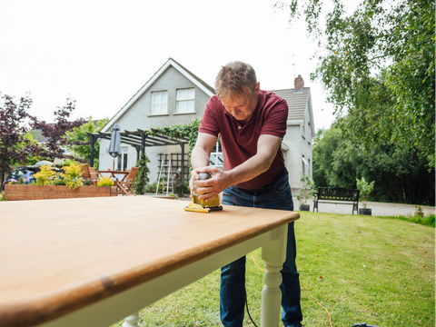 Mann som pusser ned et gammelt bord i hagen