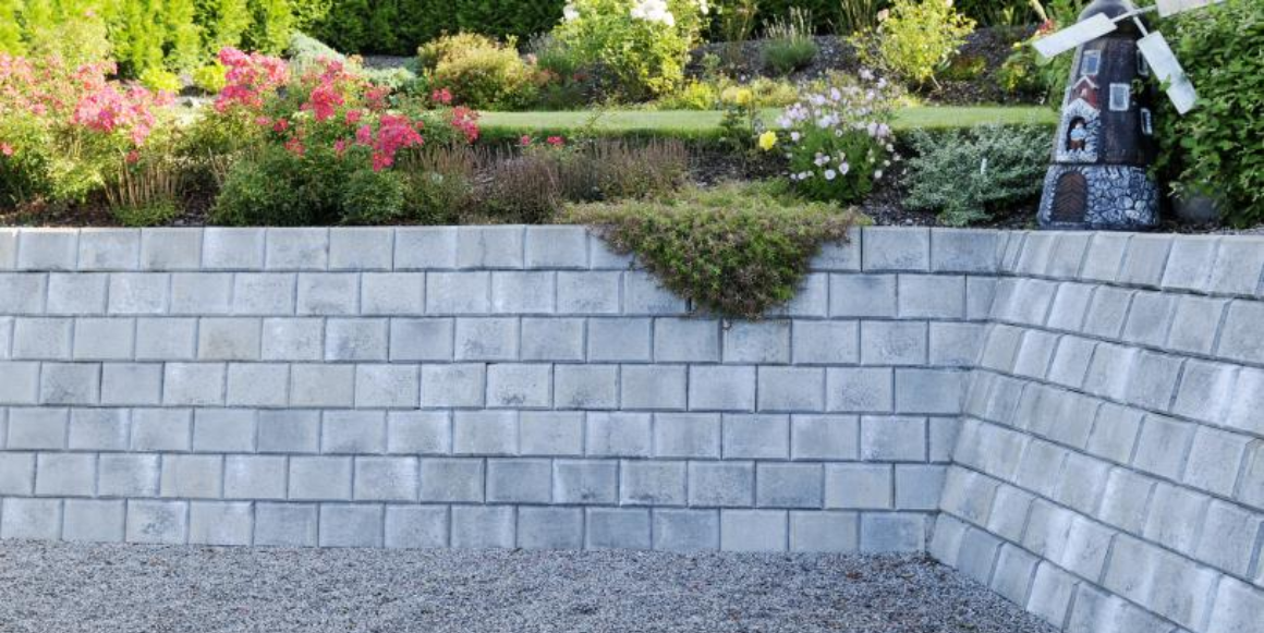 En velholdt hage med Mini Støttemur fra Aaltvedt, frodig grønt gress og livlige planter som nyter sollyset.