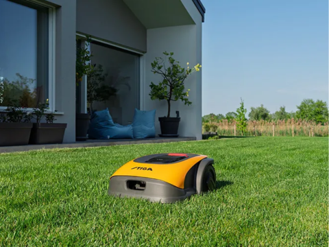 Stiga robotgressklipper i gress foran et moderne hus