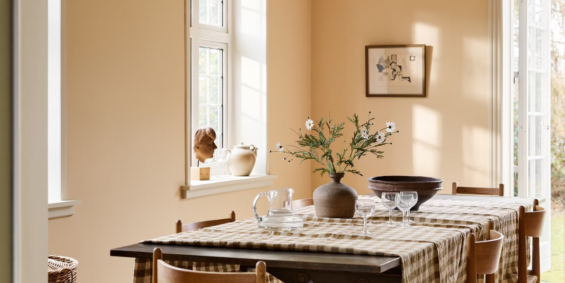 Spisestue med rutete duk foran vegg malt i Jotun 11202 Mild Ochre