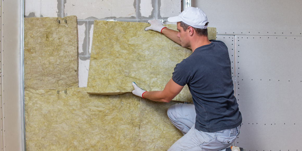 Mann som legger isolasjon inne i et hus, for å isolere og lydisolere