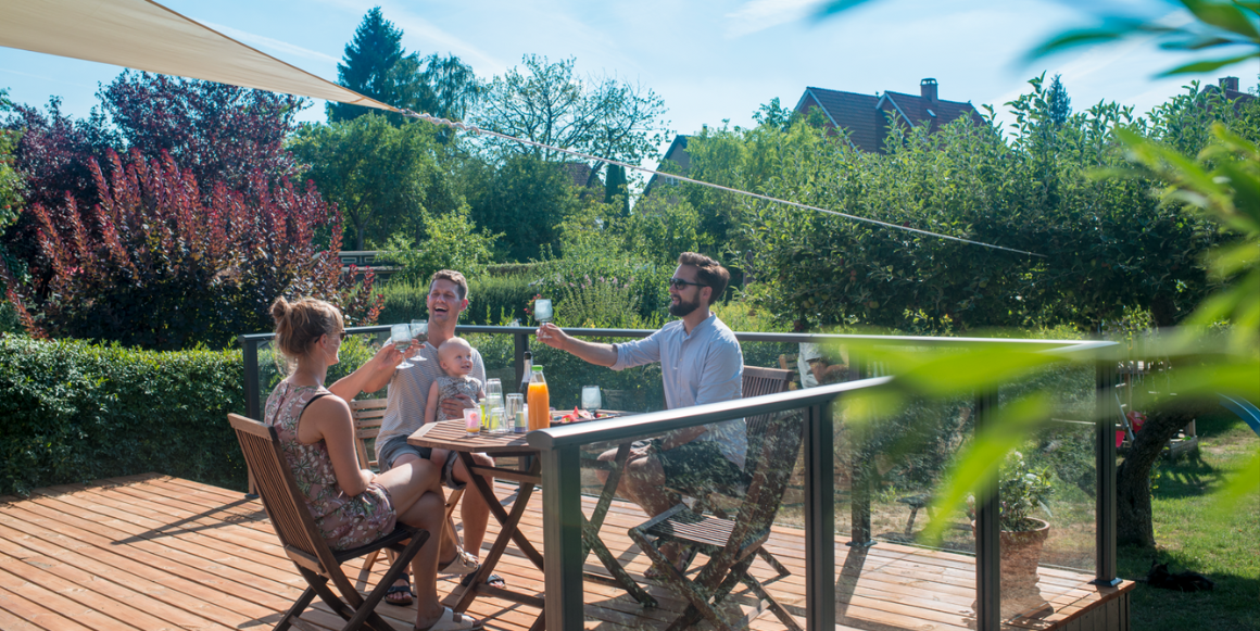 En familie sitter å hygger seg på terrassen som har et glassrekkverk fra Plastmo