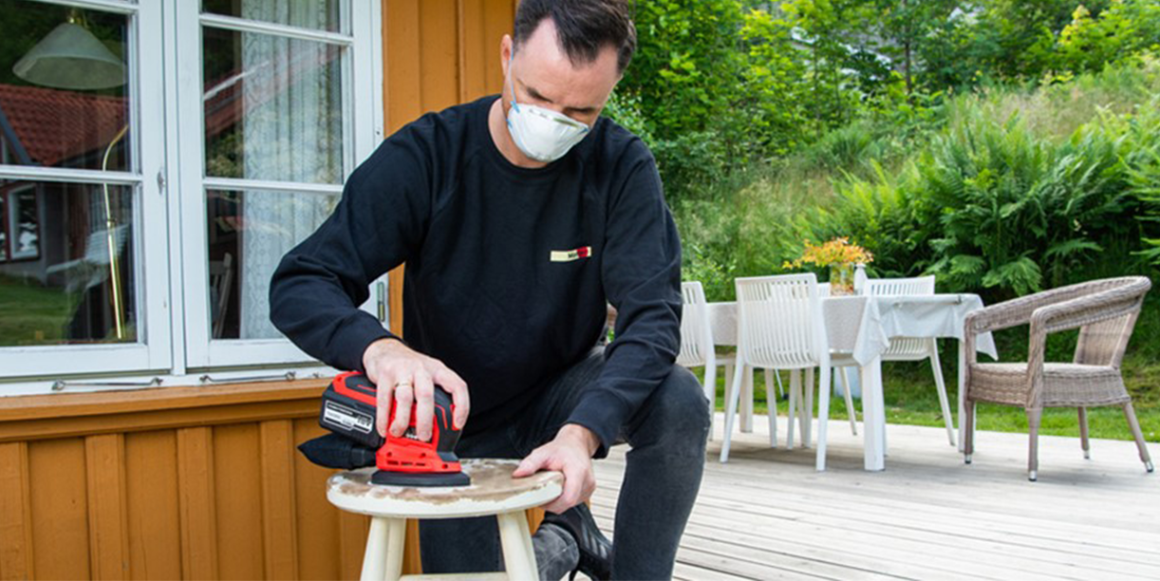 Mann sliper en krakk med en slipemaskin