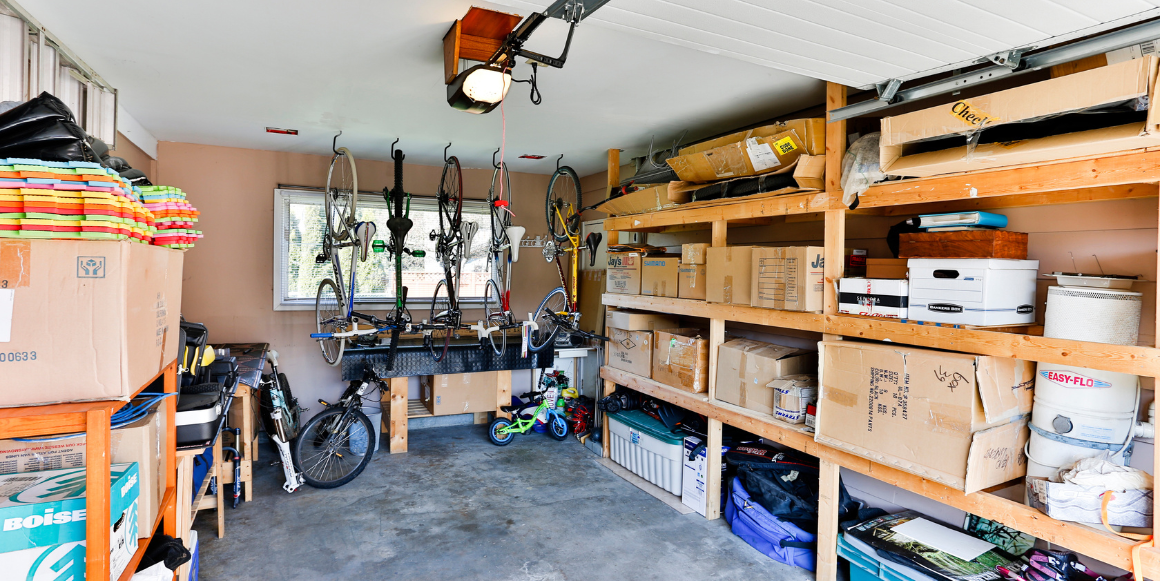 Interiør garasje. Selvbygget hyllesystem langs høyre vegg, butikkjøpte hyller langs venstre vegg og sykkeloppheng i midten.