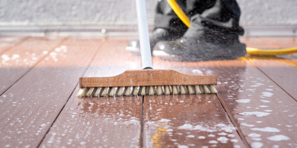 mann som vasker terrasse med kost og vannslange